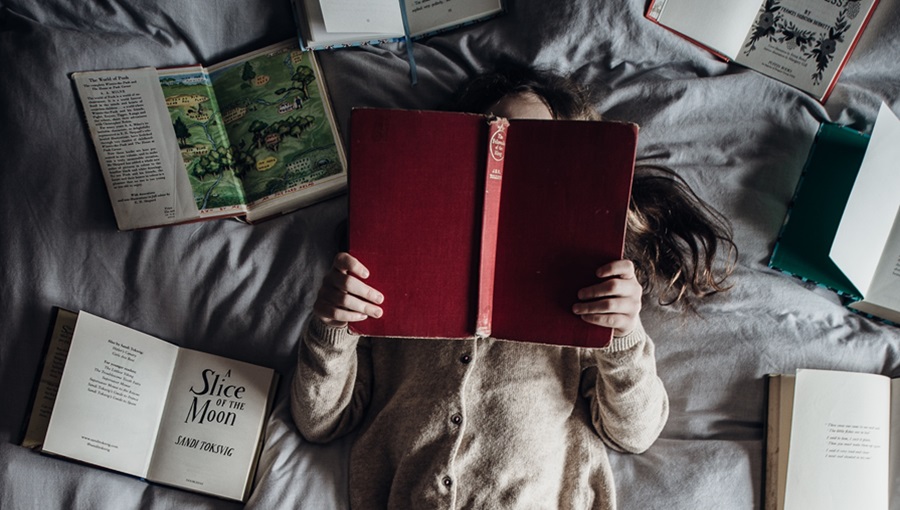 kislány olvas könyveket ágyon fekve